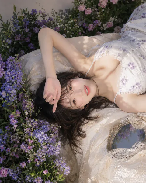 年轻女性身穿碎花吊带裙仰卧在蕾丝与紫色花丛中，俯瞰光影柔和｜通用 / 未注明 生成