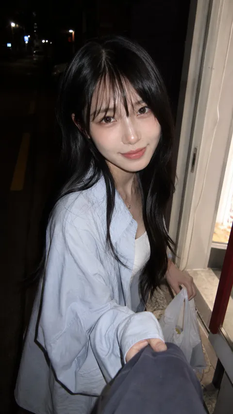 夜间便利店旁，年轻女子身穿浅蓝衬衫手提塑料袋看向镜头｜通用 / 未注明 生成